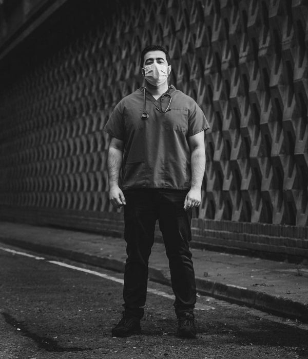 Person wearing a face mask standing against a textured wall.